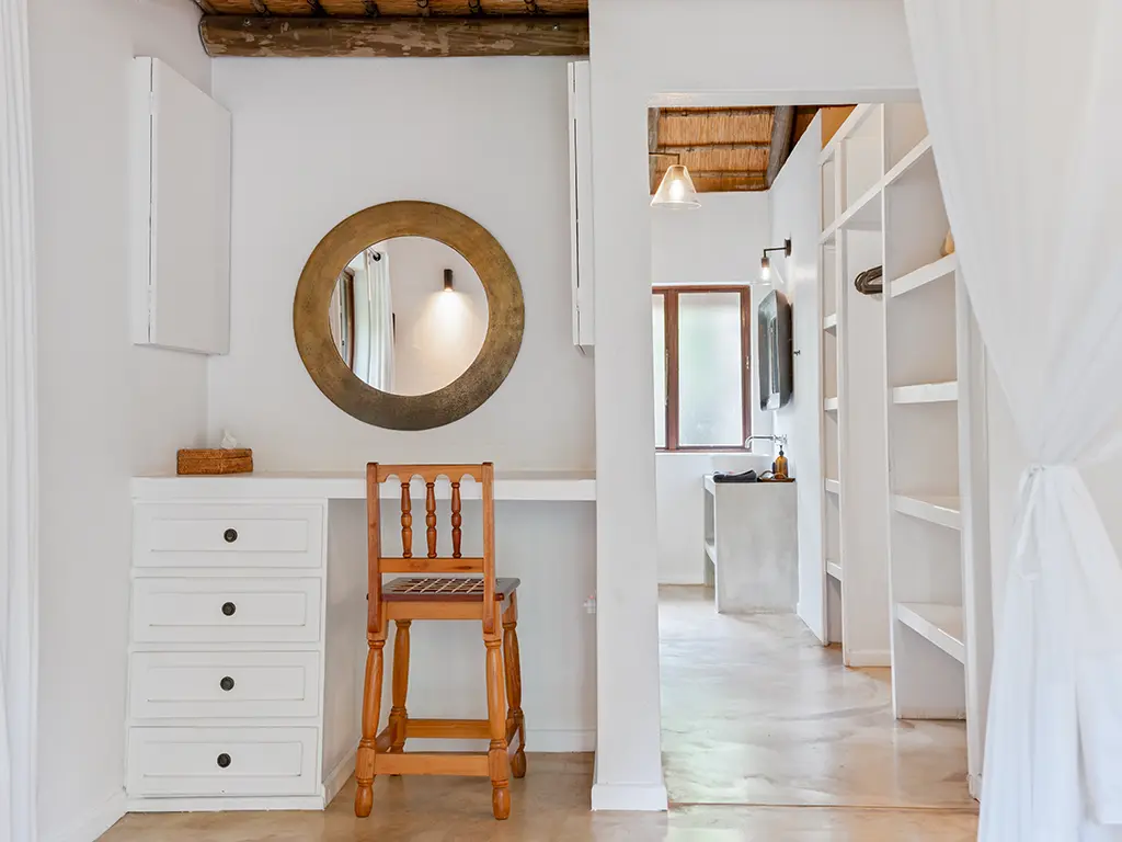 An interior view in a luxury safari Cottage at Rhino River Lodge, featuring a built-in wardrobe space on the right and a dedicated writing desk area with a large mirror.
