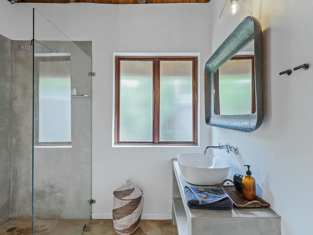 A view inside another elegant bathroom of a safari Cottage at Rhino River Lodge, showing a spacious vanity counter with a white ceramic basin, contemporary tapware, a large mirror and a spacious shower.