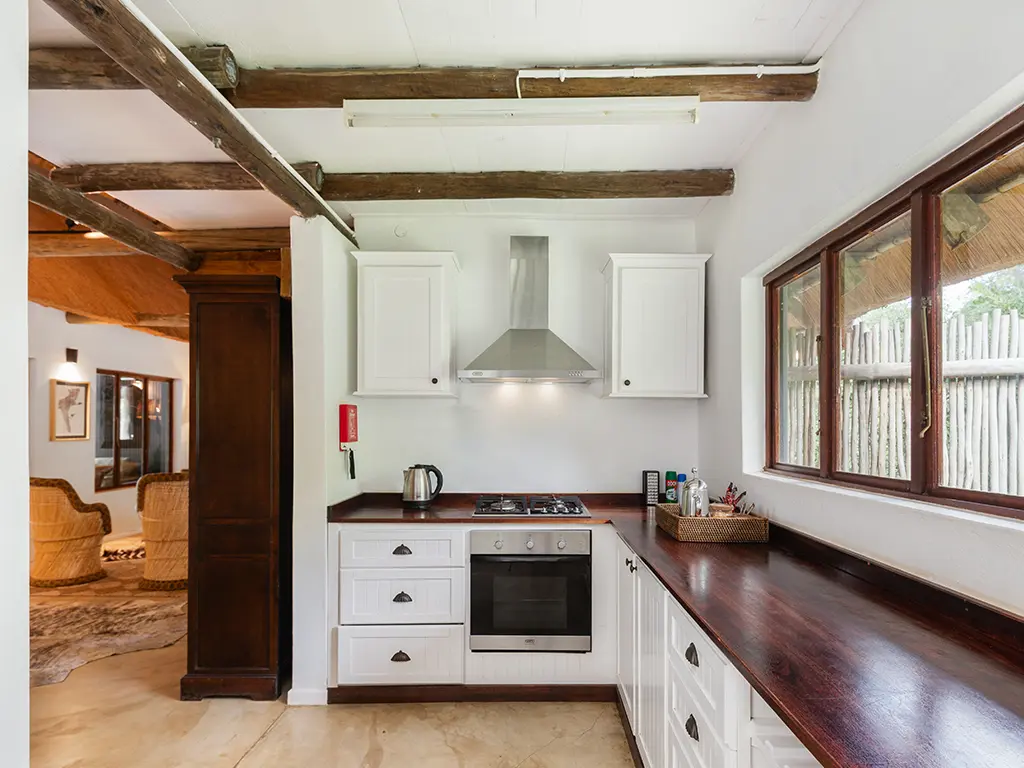 A view of the modern, fully equipped kitchen inside a luxury safari Cottage at Rhino River Lodge, featuring light-colored cabinetry, warm dark-wood countertops, and a built-in stovetop.