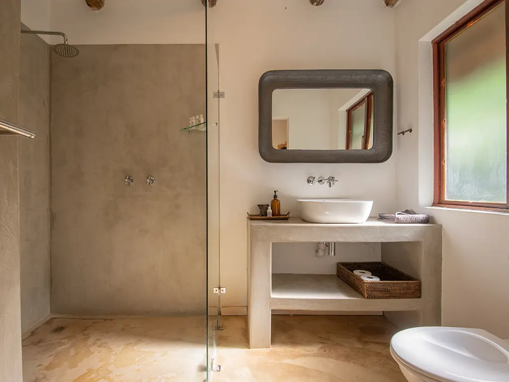 The luxurious en-suite bathroom of a safari Cottage at Rhino River Lodge, featuring an open shower with a glass partition pane, a single basin, and contemporary fixtures.