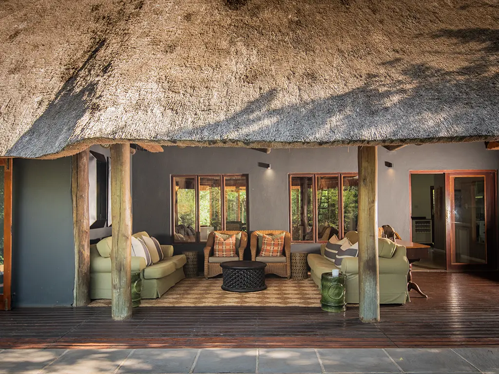 A tranquil outdoor seating area on the wooden deck of a luxury safari Cottage at Rhino River Lodge, featuring comfortable woven armchairs, sofas and a small coffee table.