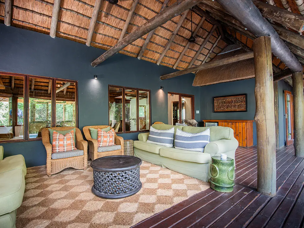 A tranquil outdoor seating area on the wooden deck of a luxury safari Cottage at Rhino River Lodge, featuring comfortable woven armchairs, sofas and a small coffee table.