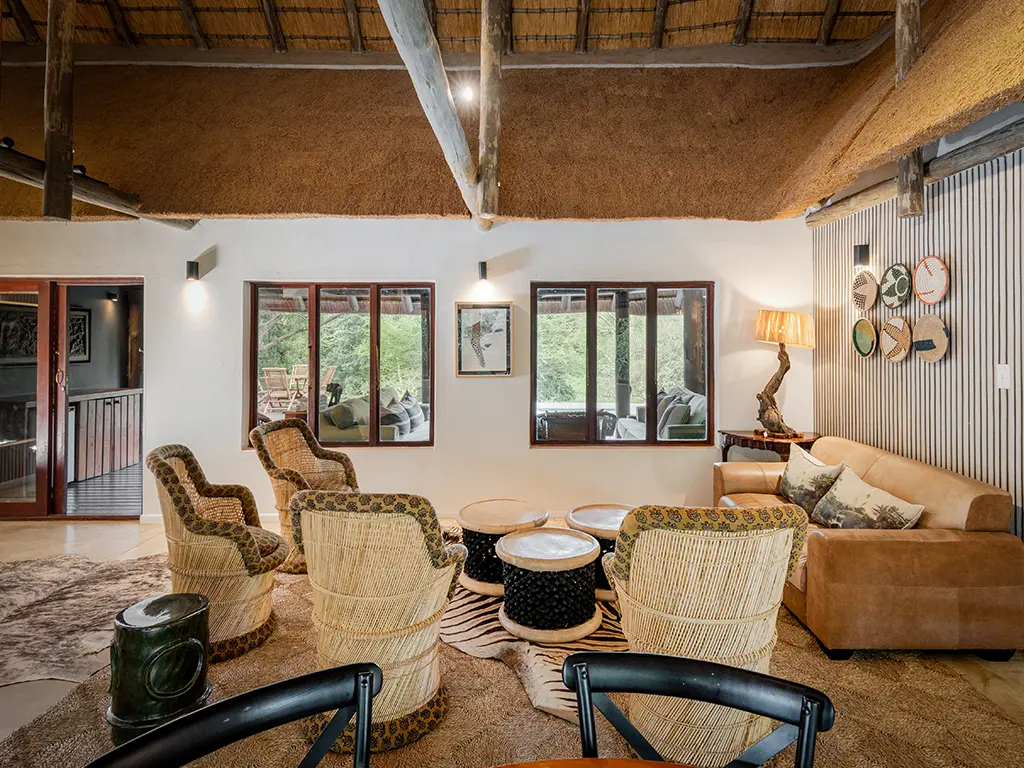 A cozy indoor lounge area inside a luxury safari Cottage at Rhino River Lodge, featuring a comfortable leather sofa, a small side table with a lamp, and warm neutral-toned decor.
