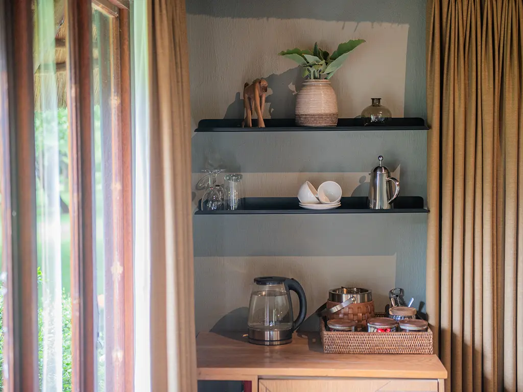 A well-equipped coffee and tea station for guests inside a luxury safari Deluxe Room at Rhino River Lodge, featuring a kettle, complimentary refreshments, neatly arranged on a wooden countertop.