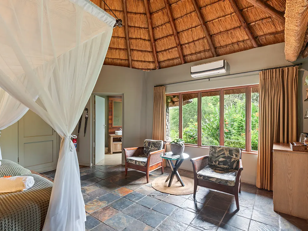 A wide interior view of a luxury safari Deluxe Room at Rhino River Lodge, showcasing a comfortable lounge area with armchairs.