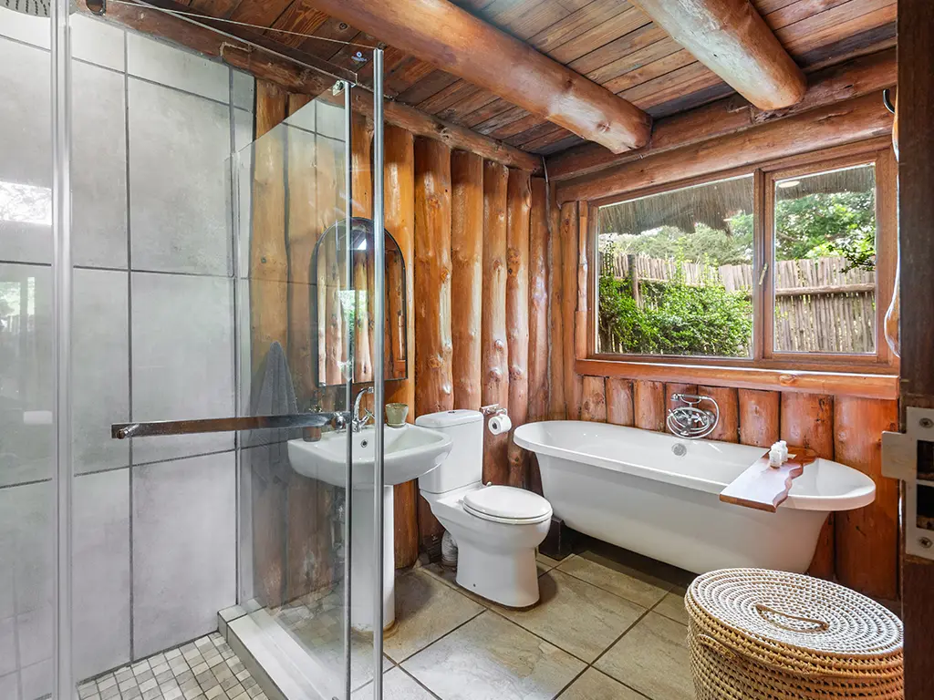 The elegant bathroom inside a Family Loft Chalet at Rhino River Lodge, featuring a spacious glass-enclosed shower, a deep freestanding soaking tub, and a single basin with a large mirror.
