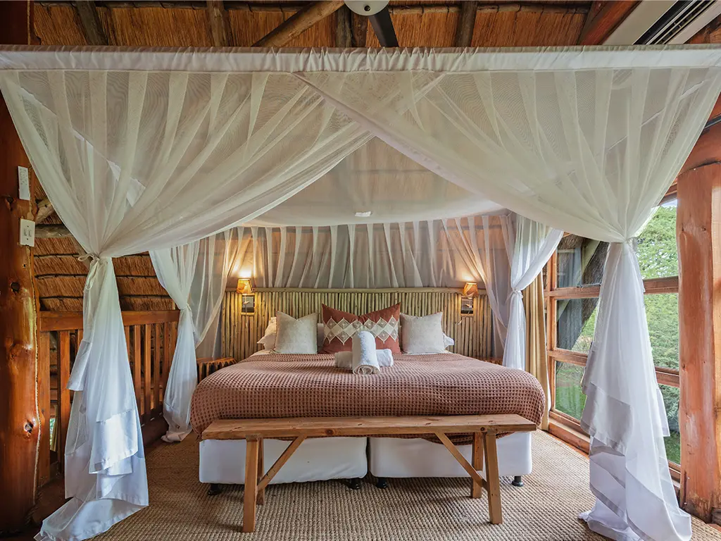 The upstairs loft bedroom inside a Family Loft Chalet at Rhino River Lodge, featuring a double bed made from two single beds pushed together, under a thatched roof structure with ambient lighting.