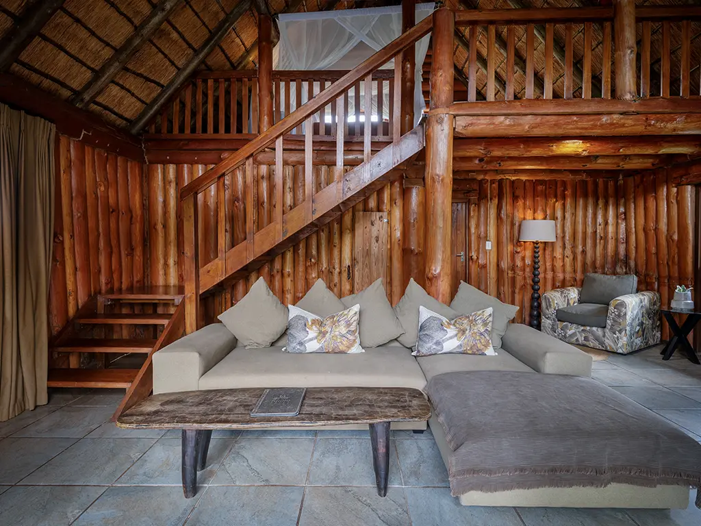 The cozy open-plan living area inside a Family Loft Chalet at Rhino River Lodge, featuring a comfortable armchair, and a plush sofa.