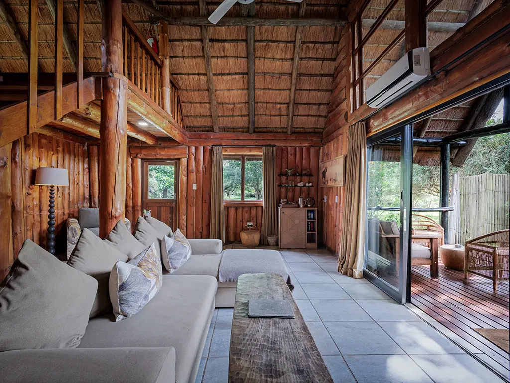 A side angle view of the living area inside a Family Loft Chalet at Rhino River Lodge, showing a plush sofa, an armchair, and a coffee and tea station in the corner, next to large glass doors opening onto an outdoor wooden deck.
