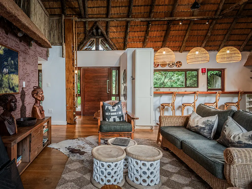 An interior view of the spacious living area and large entrance door inside the luxury safari Homestead at Rhino River Lodge, showing a elegant and comfortable seating area under high thatched ceilings.
